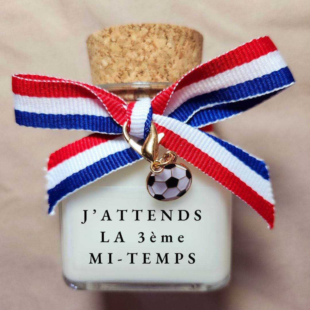 Bougie parfumée avec l'inscription humoristique et sous-entendue "J'attends la troisième mi-temps", allumée dans une atmosphère de chambre tamisée.