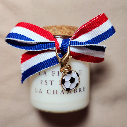 Bougie parfumée en verre avec l'inscription humoristique et coquine "La finale est dans la chambre", style supporter de football, allumée dans un décor chaleureux.