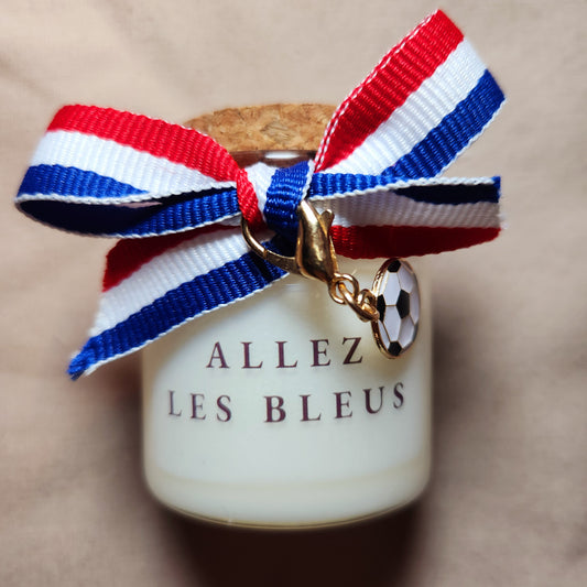 Bougie parfumée de supporter avec l'inscription "Allez les Bleus" en lettres capitales, allumée sur une table basse pour encourager l'équipe de France.
