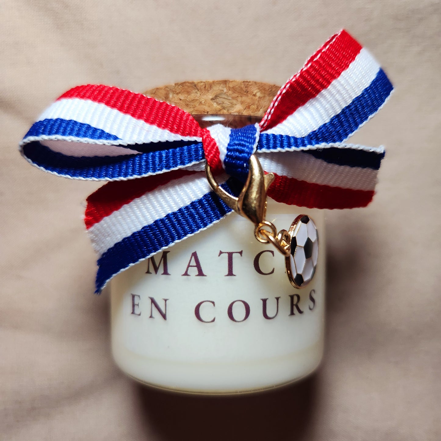 Bougie parfumée avec l'inscription "Match en cours" entourée de motifs de ballons de foot, allumée sur une table de salon.