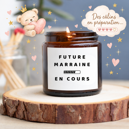 Bougie allumée en pot ambré avec le message Future marraine en cours et une barre de chargement, entourée d’un ourson, de cœurs roses et d’étoiles dorées.