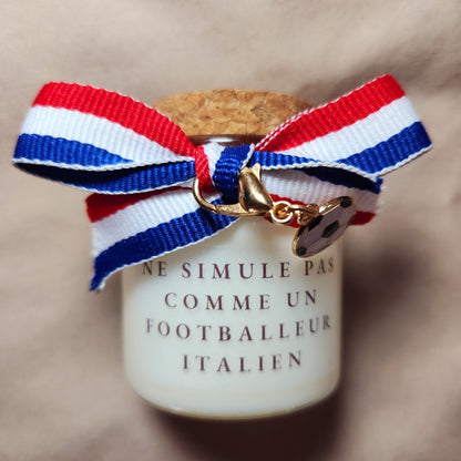Bougie parfumée humoristique avec l'inscription "Ne simule pas comme un joueur italien", style supporter de football, allumée sur une table.