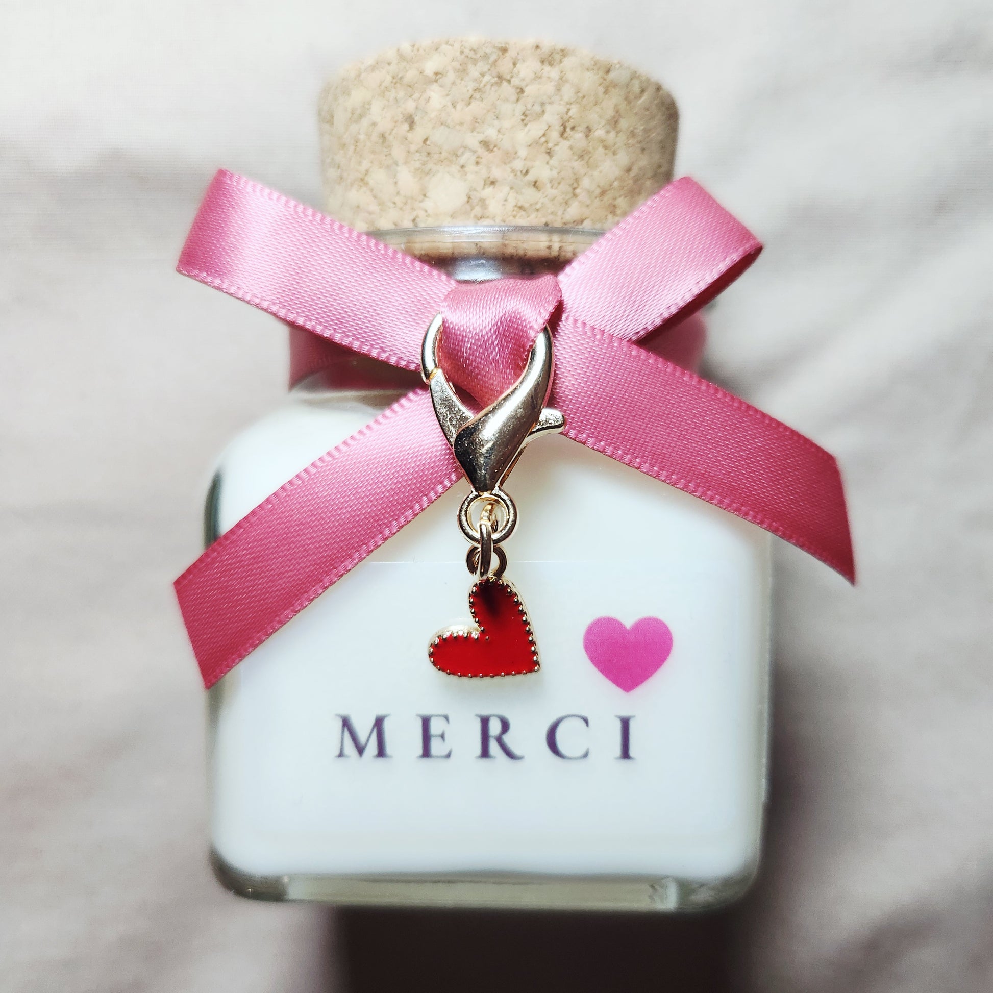 Bougie parfumée artisanale avec l'inscription Merci suivie d'un joli cœur rouge, allumée dans une atmosphère douce et chaleureuse.