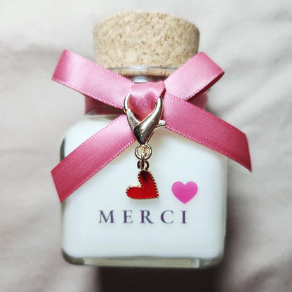 Bougie parfumée artisanale avec l'inscription Merci suivie d'un joli cœur rouge, allumée dans une atmosphère douce et chaleureuse.