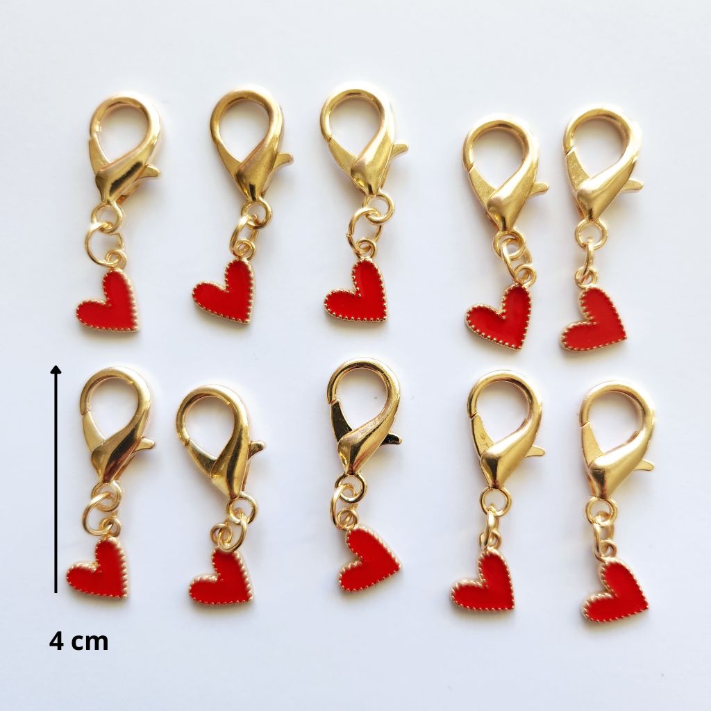 Pendentif en forme de larme dorée abritant un magnifique cœur rouge vif suspendu à un mousqueton.