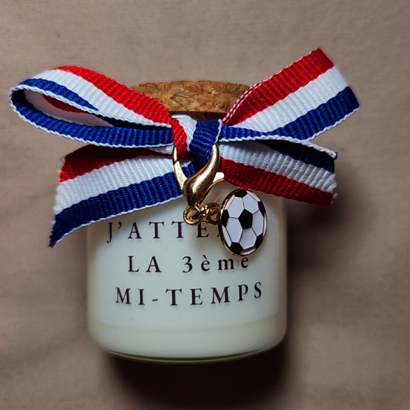 Bougie parfumée artisanale portant l'inscription coquine "J'attends la troisième mi-temps" avec des illustrations de football, allumée dans une ambiance de chambre ou de salon cosy mamiecandle