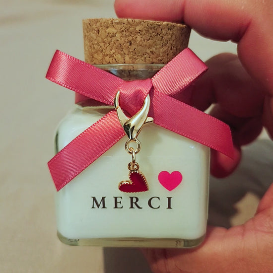 Bougie parfumée artisanale avec l'inscription Merci suivie d'un joli cœur rouge, allumée dans une atmosphère douce et chaleureuse.mamiecandle