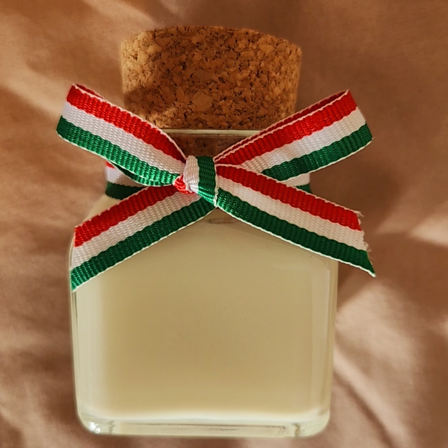 Bougie parfumée artisanale inspirée de l'Italie, décorée d'un ruban tricolore aux couleurs du drapeau italien, allumée dans un intérieur ensoleillé.