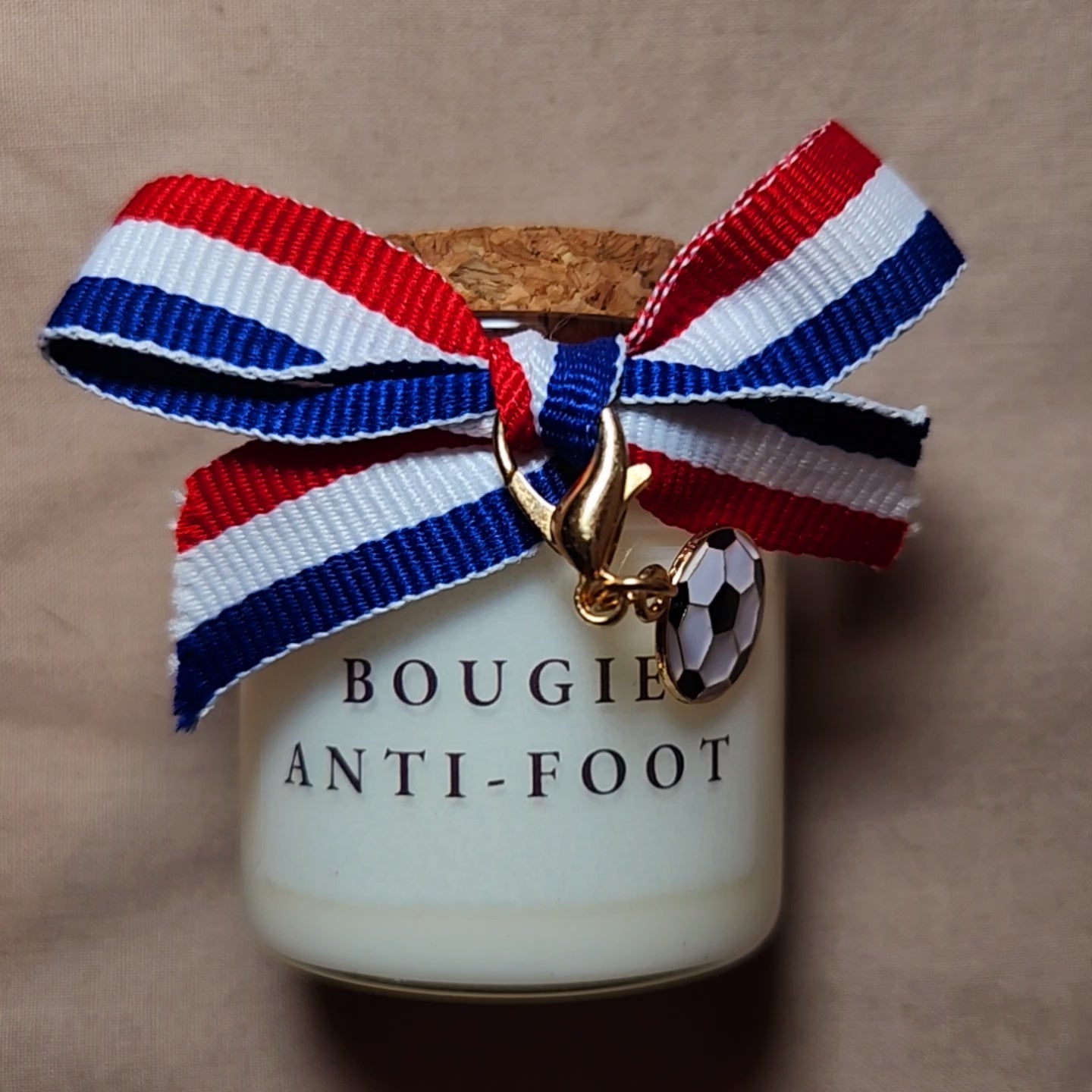 Bougie parfumée humoristique avec l'inscription "Bougie anti foot", allumée dans un salon calme loin des écrans. mamiecandle