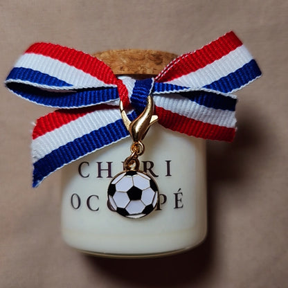 Bougie parfumée en verre avec l'inscription "Chéri Occupé" et des dessins de football, allumée sur une table basse en bois pendant une soirée match devant la télévision mamiecandle