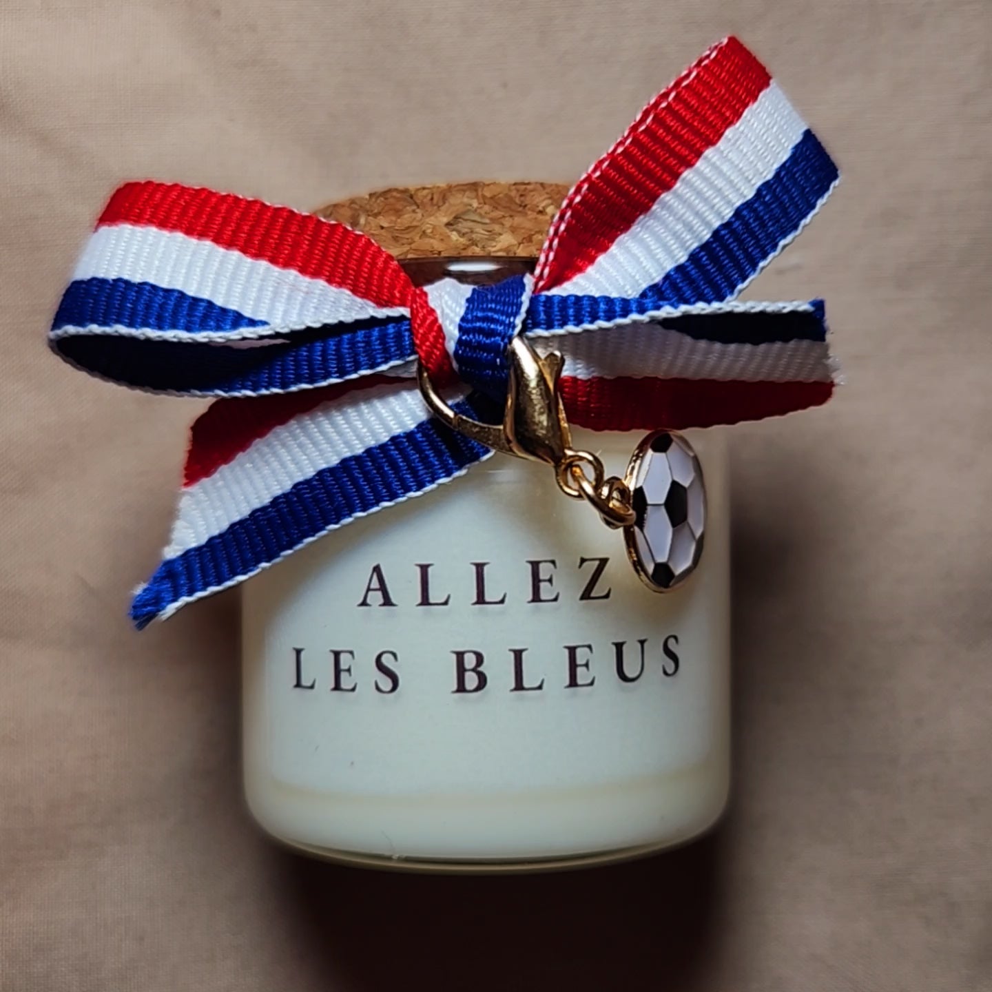 Bougie parfumée de supporter avec l'inscription "Allez les Bleus" en lettres capitales, allumée sur une table basse pour encourager l'équipe de France. mamiecandle