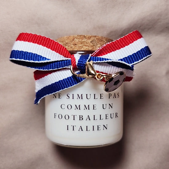 Bougie parfumée humoristique avec l'inscription "Ne simule pas comme un joueur italien", style supporter de football, allumée sur une table. mamiecandle