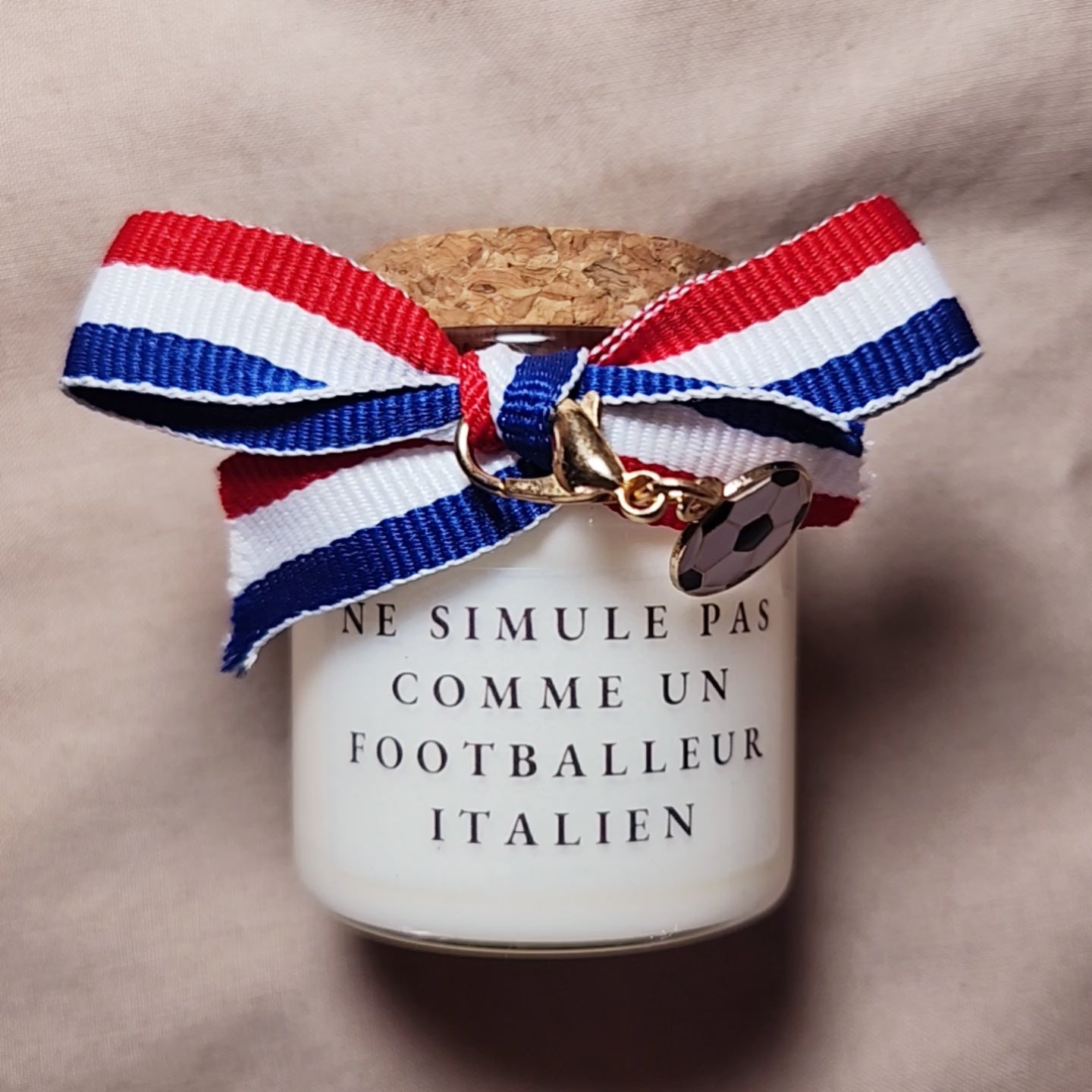 Bougie parfumée humoristique avec l'inscription "Ne simule pas comme un joueur italien", style supporter de football, allumée sur une table. mamiecandle