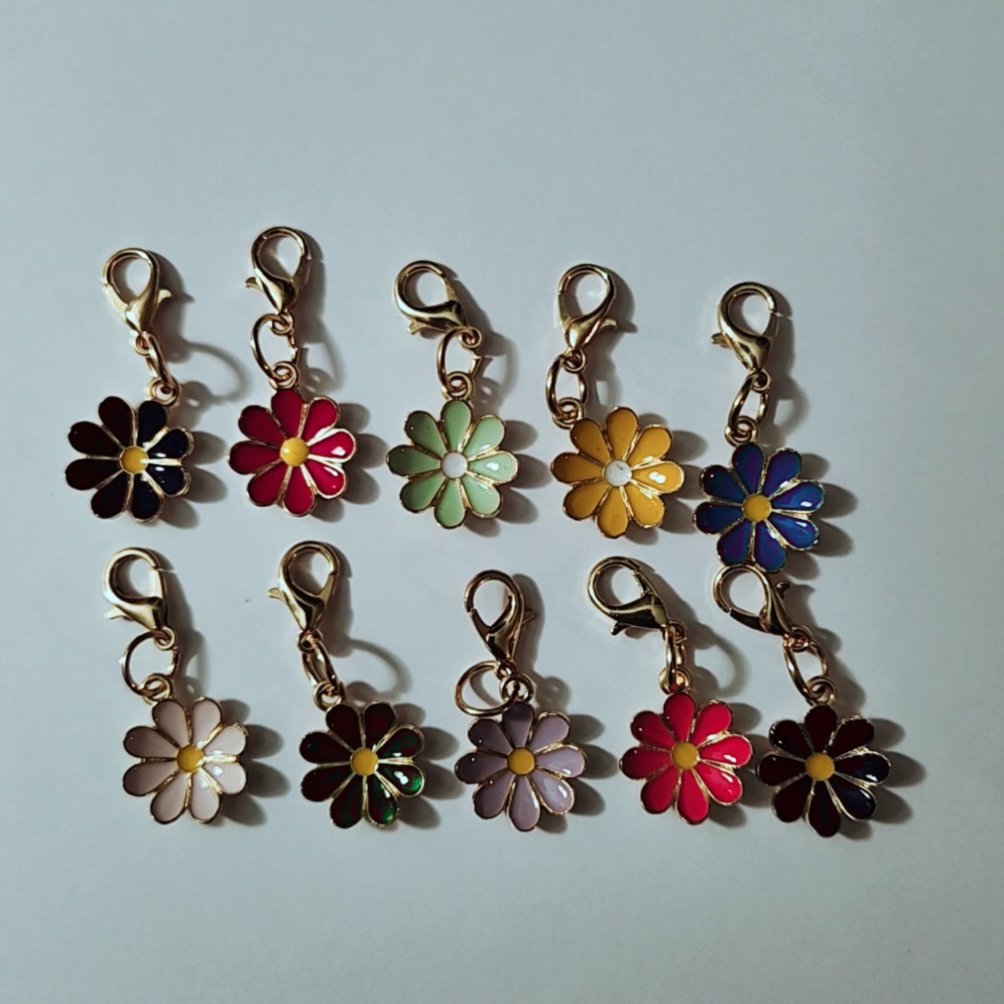 Assortiment de pendentifs en forme de fleurs de marguerites colorées en émail avec contours dorés et fermoirs mousquetons, d'après le fichier fleurs.mamiecandle